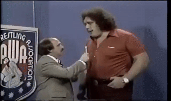 Andre the Giant hold his hand up to much shorter sportscaster.