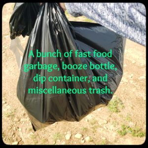 Amber holding up a black trash bag from picking up litter at the park.