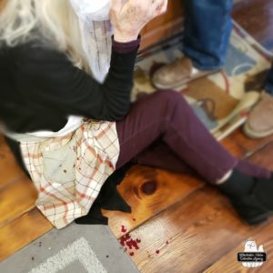 The Cook on the kitchen floor immediately after the fall; blood all over while she holds ice and towels to her head.