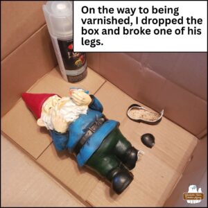 2025 garden gnome, Gnomez Addams in a box with broken boot pieces and spray paint can of varnish. "On the way to being varnished, I dropped the box and broke one of his legs."