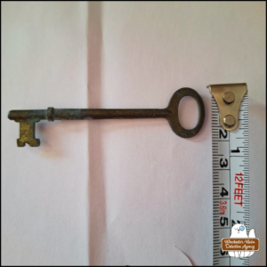 a skeleton key on a white background next to a measuring tape showing approximate width of the handle end 2cm