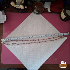 two strings of (plastic) purplish-pink gems on a white paper towel next to a measuring tape showing them close to 15 cm