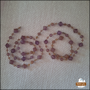 two strings of (plastic) purplish-pink gems in spirals on a white paper towel