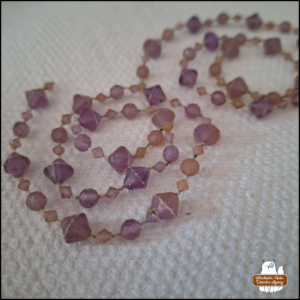 two strings of (plastic) purplish-pink gems in spirals on a white paper towel
