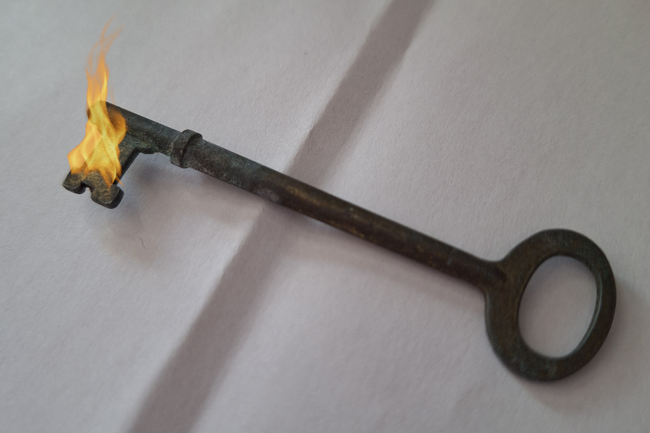 an antique skeleton key on white paper. the key's locking end has special effects flames coming from it.