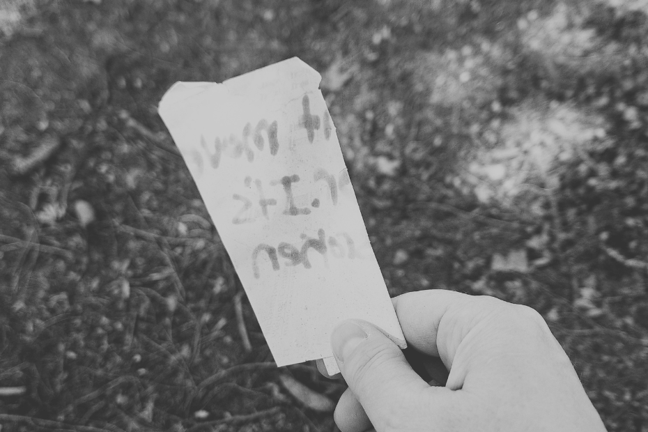 in black and white, Amber's hand holding a note discovered on the ground. Text that's visible appears to be written with marker.