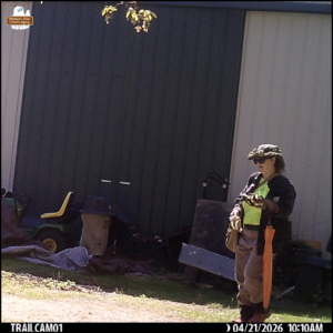 Amber carrying the dead red squirrel in a gloved hand at the back of a building in bright sunlight