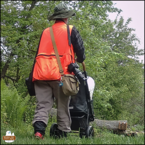 day time (color) trailcam photo of the back of Amber pushing Ollie's stroller through the grass